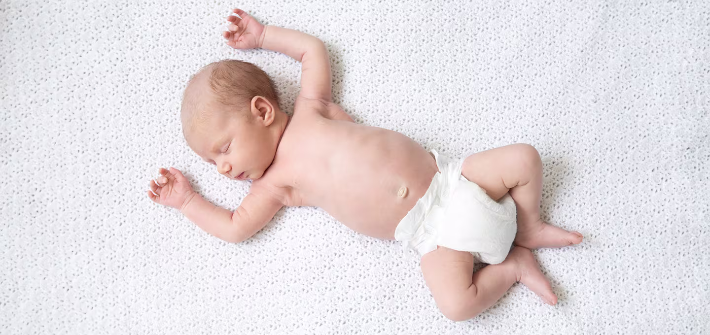 A newborn baby sleeping on its back, wearing just a diaper