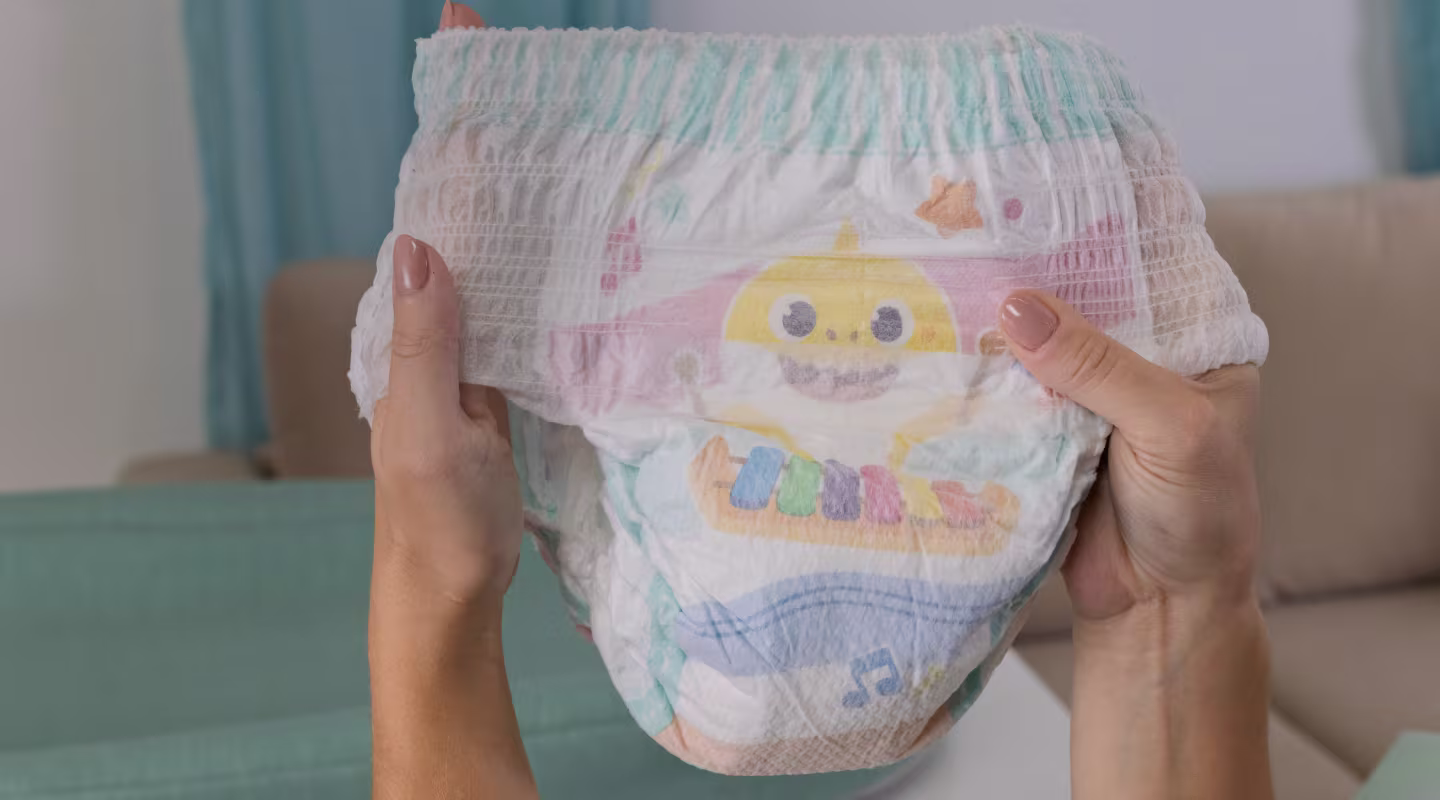 Dos manos sosteniendo un pañal de entrenamiento Pampers Pure mostrando la pretina elástica que ayuda a proteger contra fugas y garantiza un ajuste cómodo.