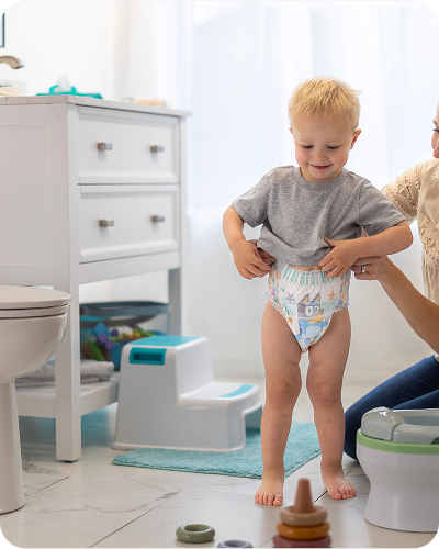Mom helping her smiling son pull up a fresh Easy Ups training pant in the bathroom as he starts his potty training journey 