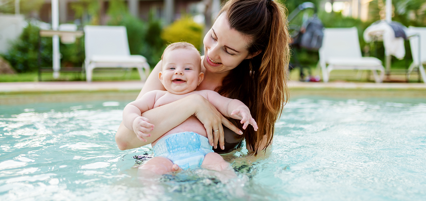 A caregiver holding a baby in a pool, and the baby is wearing a swim diaper.