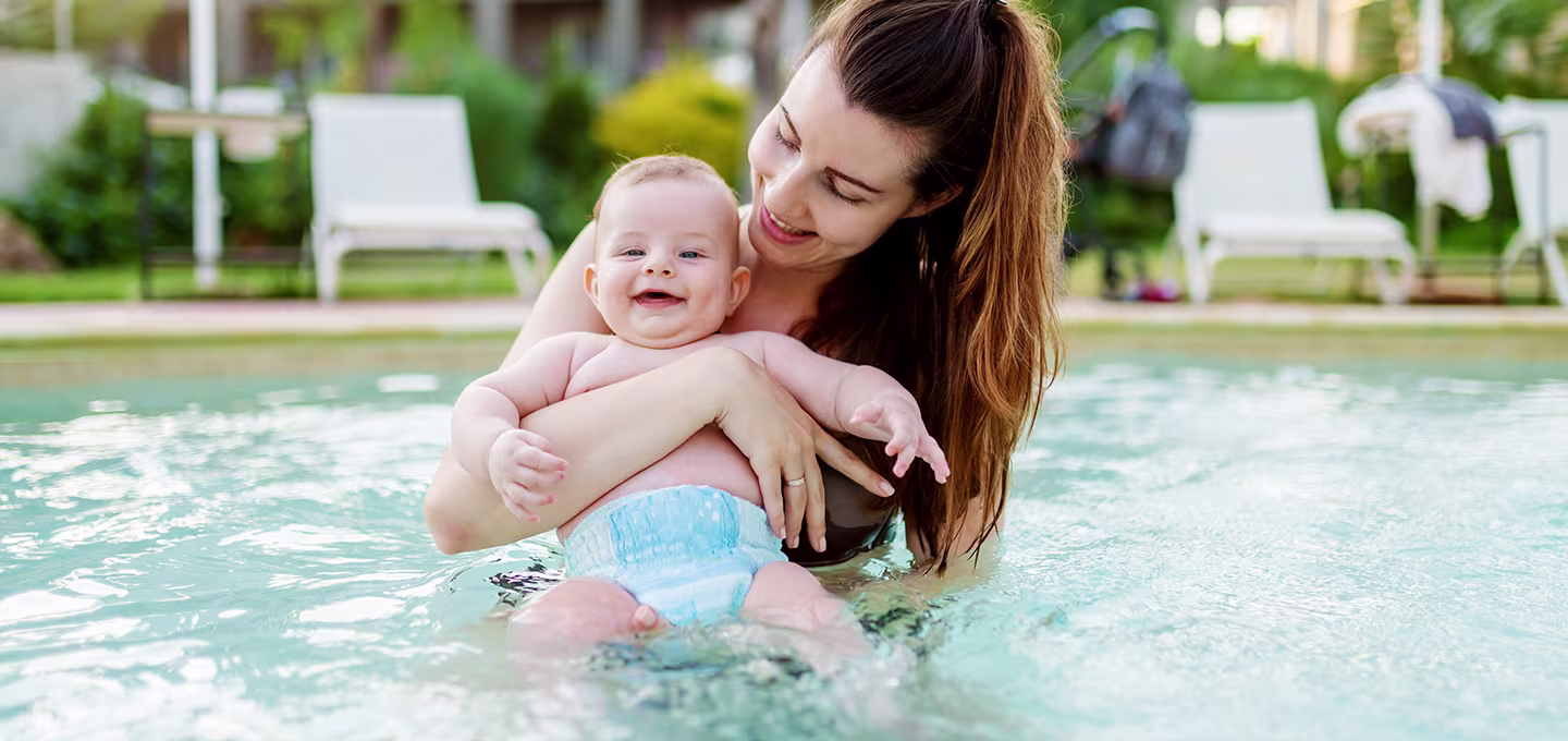 A caregiver holding a baby in a pool, and the baby is wearing a swim diaper.