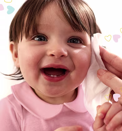 Et nærbilde av et spedbarns ansikt mens en hånd forsiktig tørker kinnet deres med en Pampers Sensitive New Baby-våtserviett. Et nærbilde av et spedbarns ansikt mens en hånd forsiktig tørker kinnet deres med en Pampers Sensitive New Baby-våtserviett.