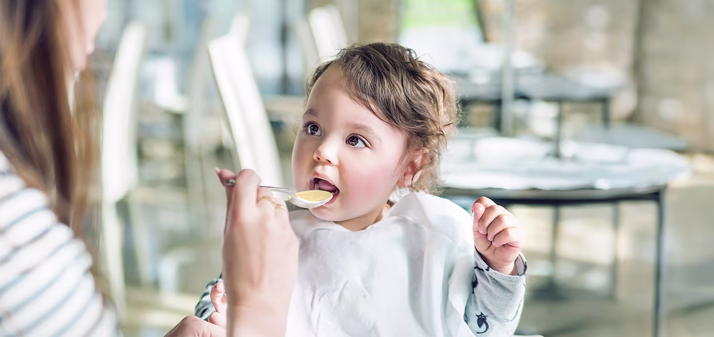 Parent donnant une cuillère de purée à un bébé, illustrant l’alimentation et la question du miel avant 1 an.