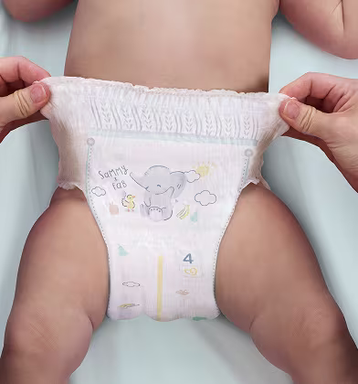 A baby wearing a white nappy pant and two hands pull on the top edge of the nappy pant, stretching it.