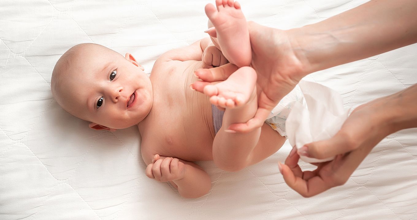 Imagine cu un bebeluș în pat, care este șters cu un șervețel umed Pampers Sensitive 0% Plastic.