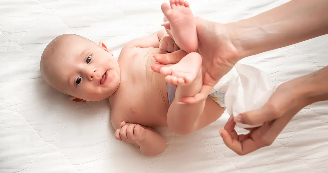 Imagine cu un bebeluș în pat, care este șters cu un șervețel umed Pampers Sensitive 0% Plastic.