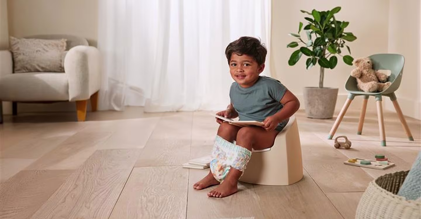 Un niño pequeño está sentado en un pequeño y colorido orinal en un baño bien iluminado.