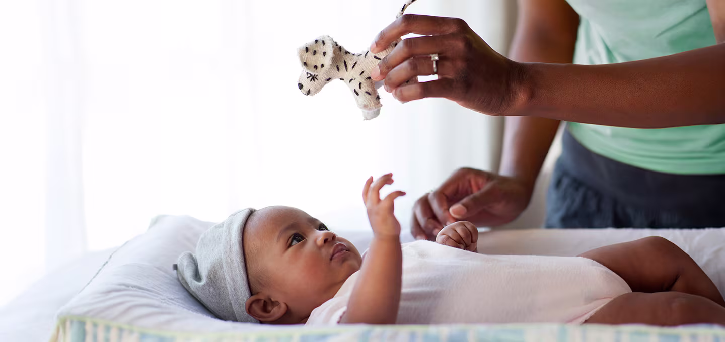 Baby lying on a changing table reaches up toward a small toy, practicing focusing and visual tracking.
