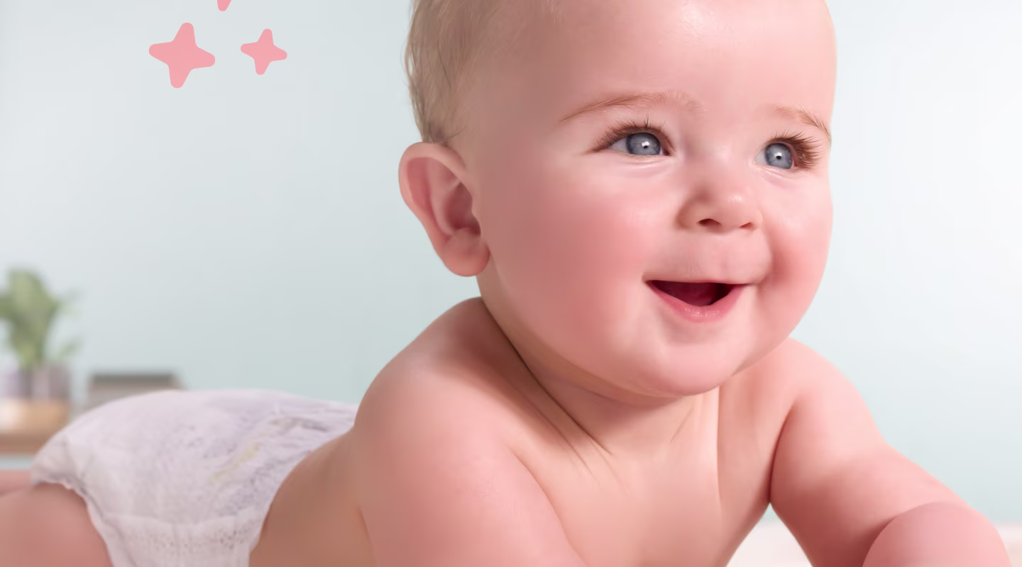A happy baby with blue eyes wearing a white diaper lies on its stomach and smiles while looking up and to the side.
