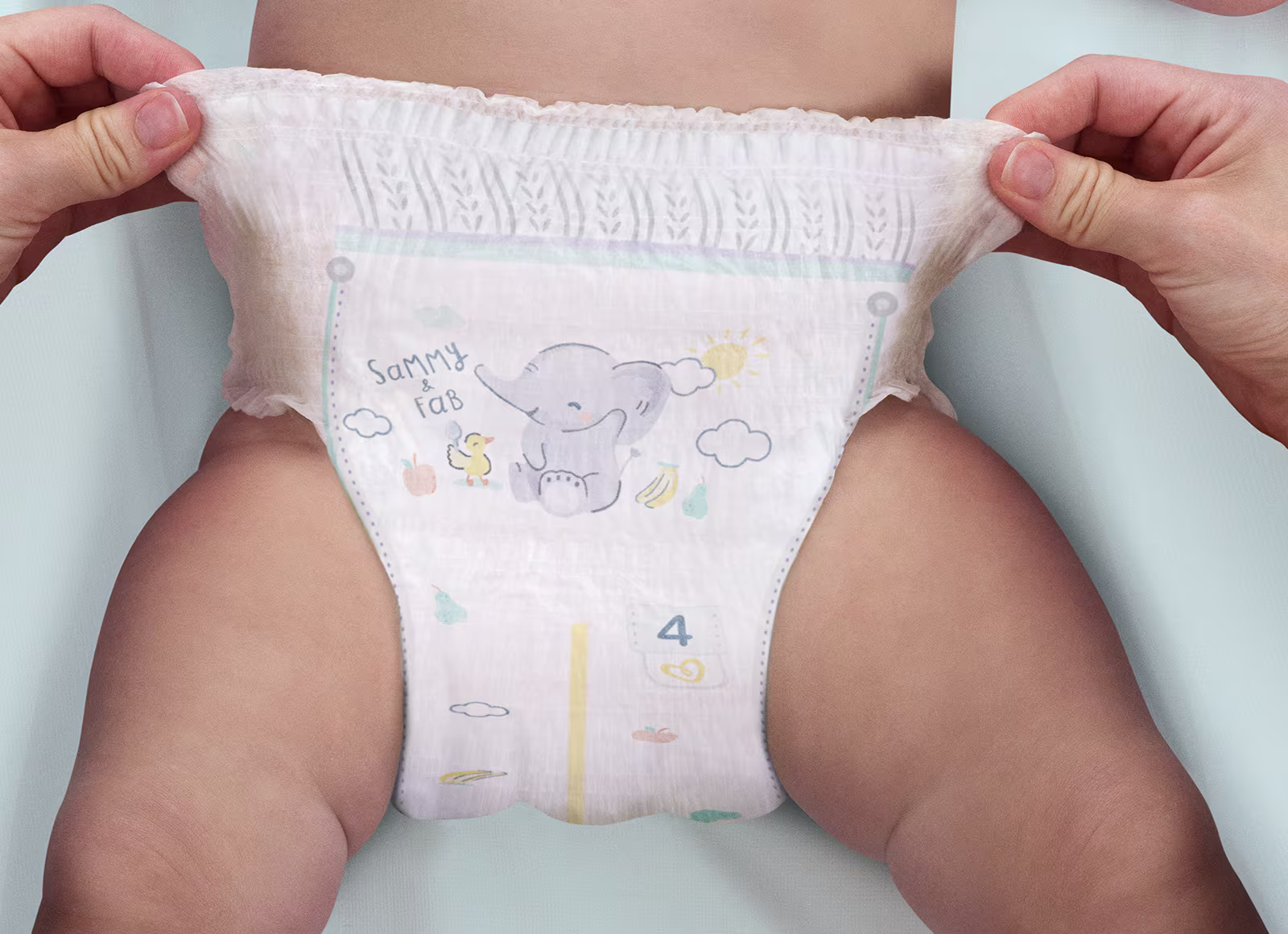 Un bébé porte une Pampers® Premium Protection™ Pants et 2 mains illustrent la facilité d’enfiler la couche comme un sous-vêtement.