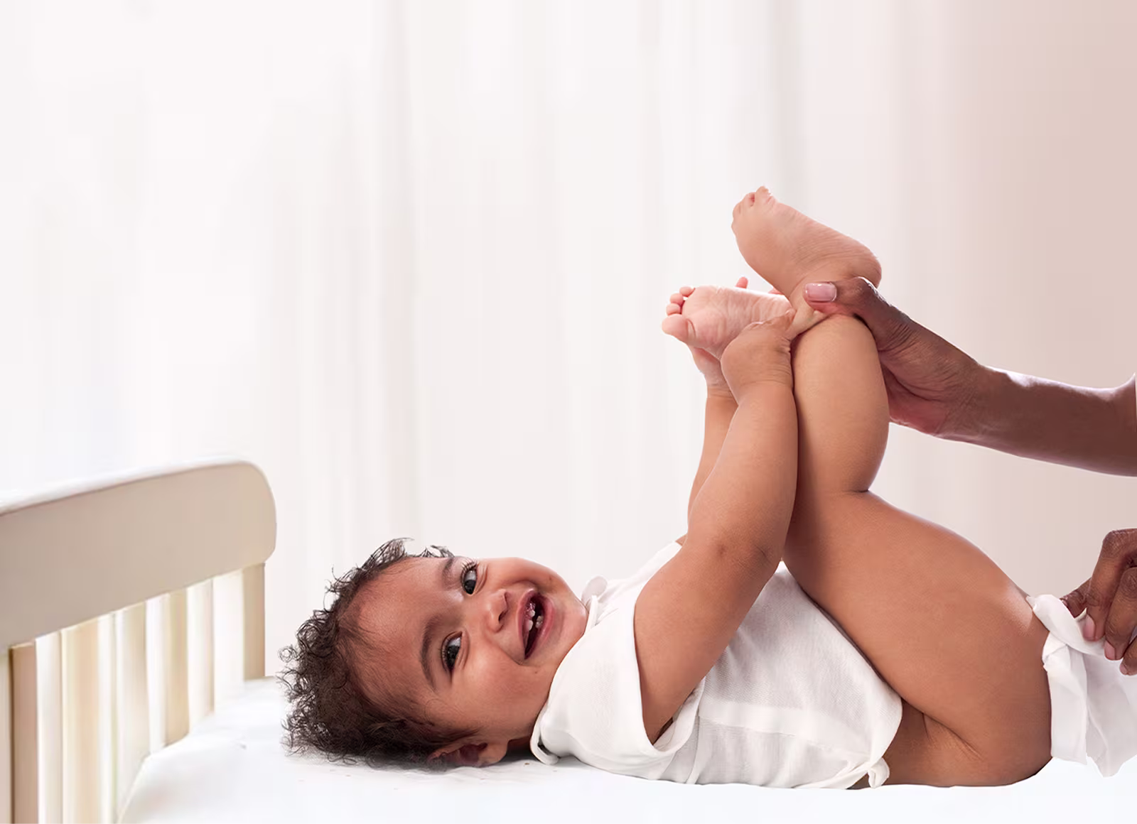 Un bebé yace de espaldas sobre una superficie blanca, levantando los pies mientras un padre utiliza una toallita para limpiar el trasero del bebé. Un bebé yace de espaldas sobre una superficie blanca, levantando los pies mientras un padre utiliza una toallita para limpiar el trasero del bebé.