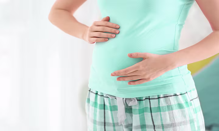 Persona embarazada tocando su abdomen con ambas manos, mostrando atención a los primeros movimientos fetales conocidos como quickening