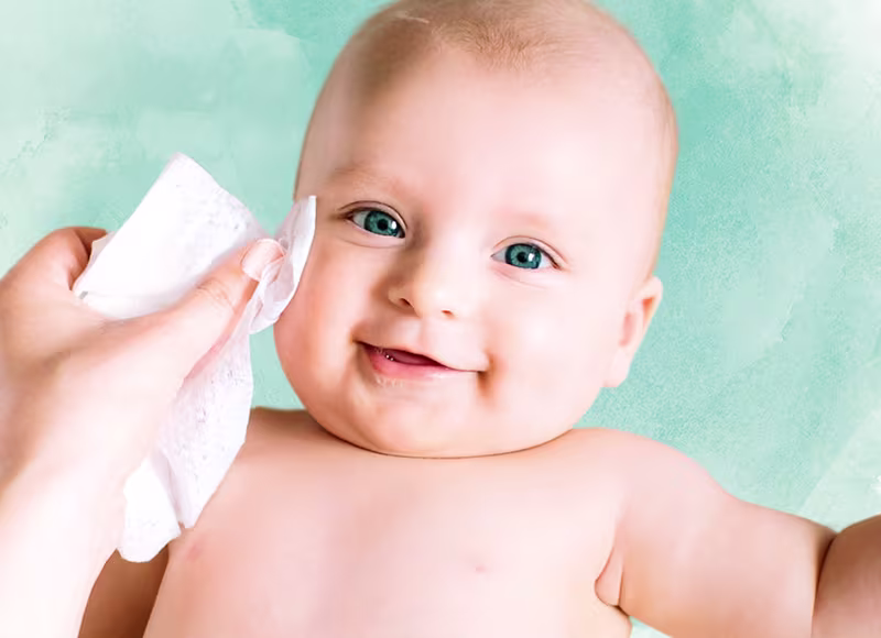 En närbild av ett babys ansikte medan en hand försiktigt torkar deras kind med en Pampers Harmonie Aqua-wipe.