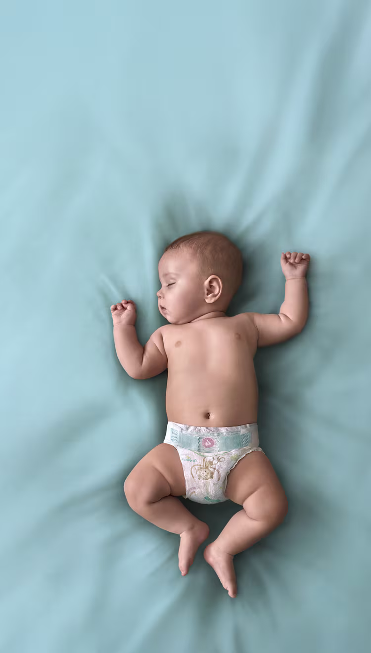 Un bébé est allongé sur le dos sur une couverture turquoise et porte une couche Pampers Baby-Dry.