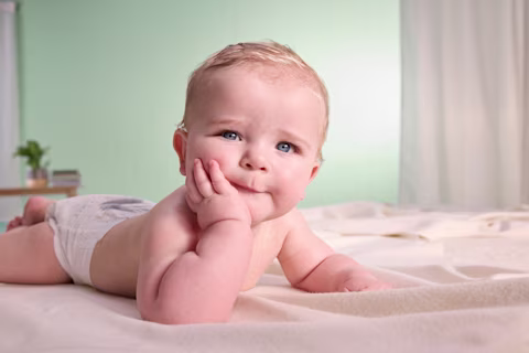 Bebé acostado boca abajo usando Pampers Swaddlers con una mano descansando bajo su barbilla