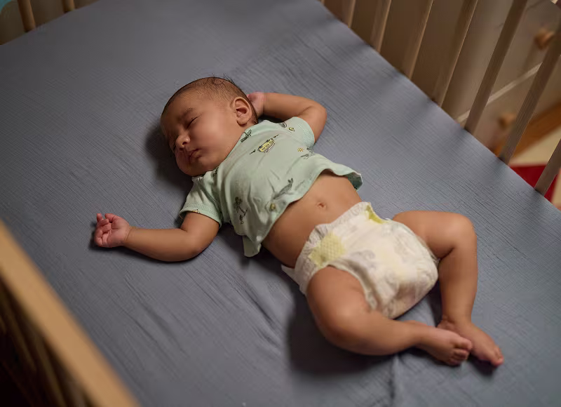 Baby sleeping peacefully in the crib wearing Pampers Swaddlers and a green shirt