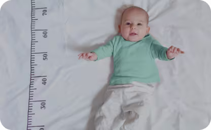 Baby lying on bed next to measurement line smiling