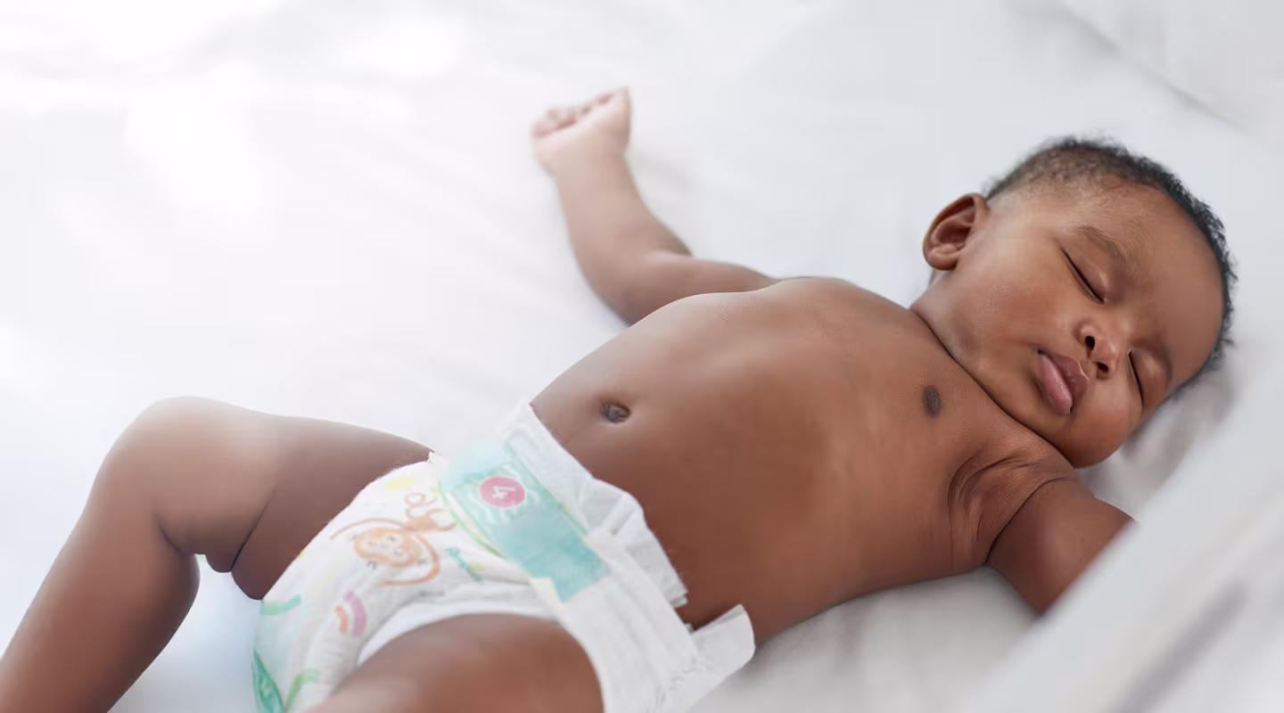 A baby sleeps on their back wearing a Pampers nappy
