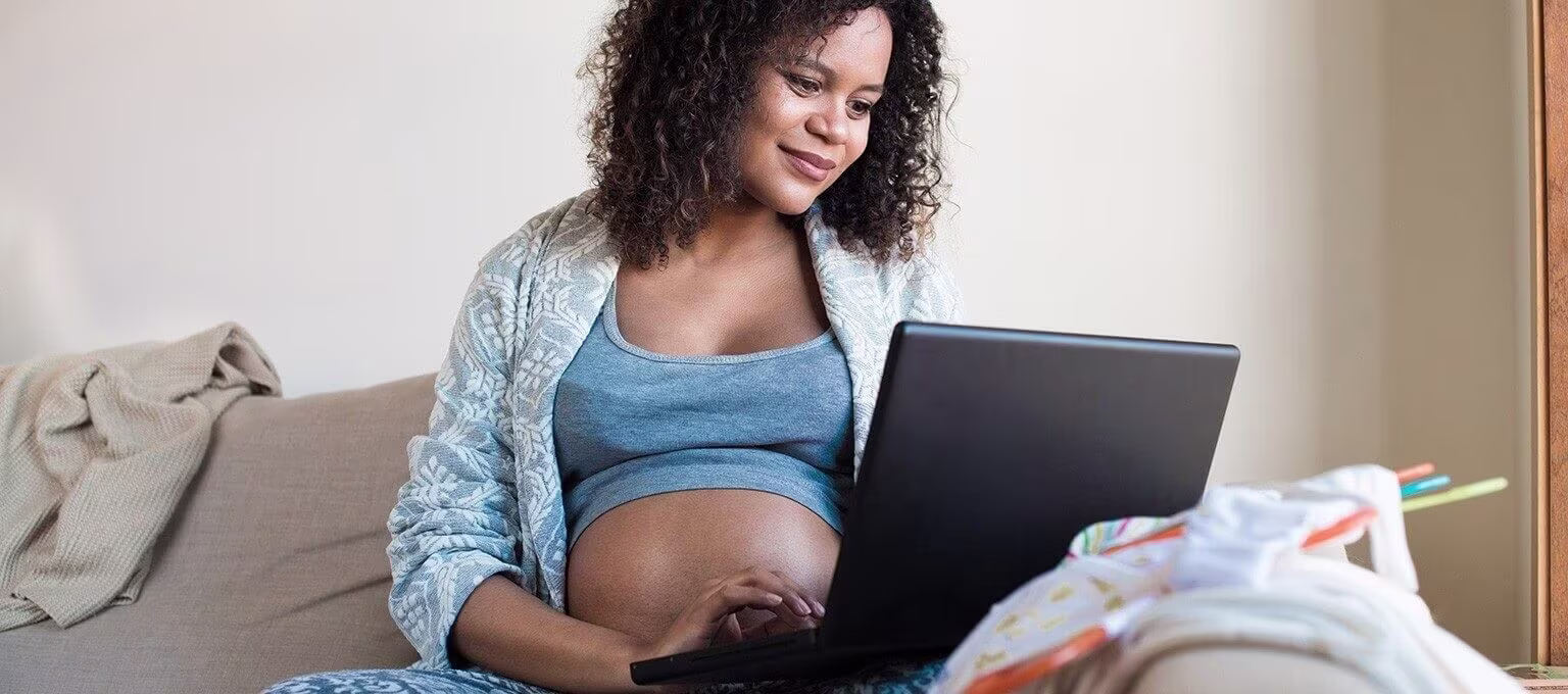 Pregnant woman seated with a computer, preparing or researching her birth plan