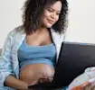 Pregnant woman seated with a computer, preparing or researching her birth plan