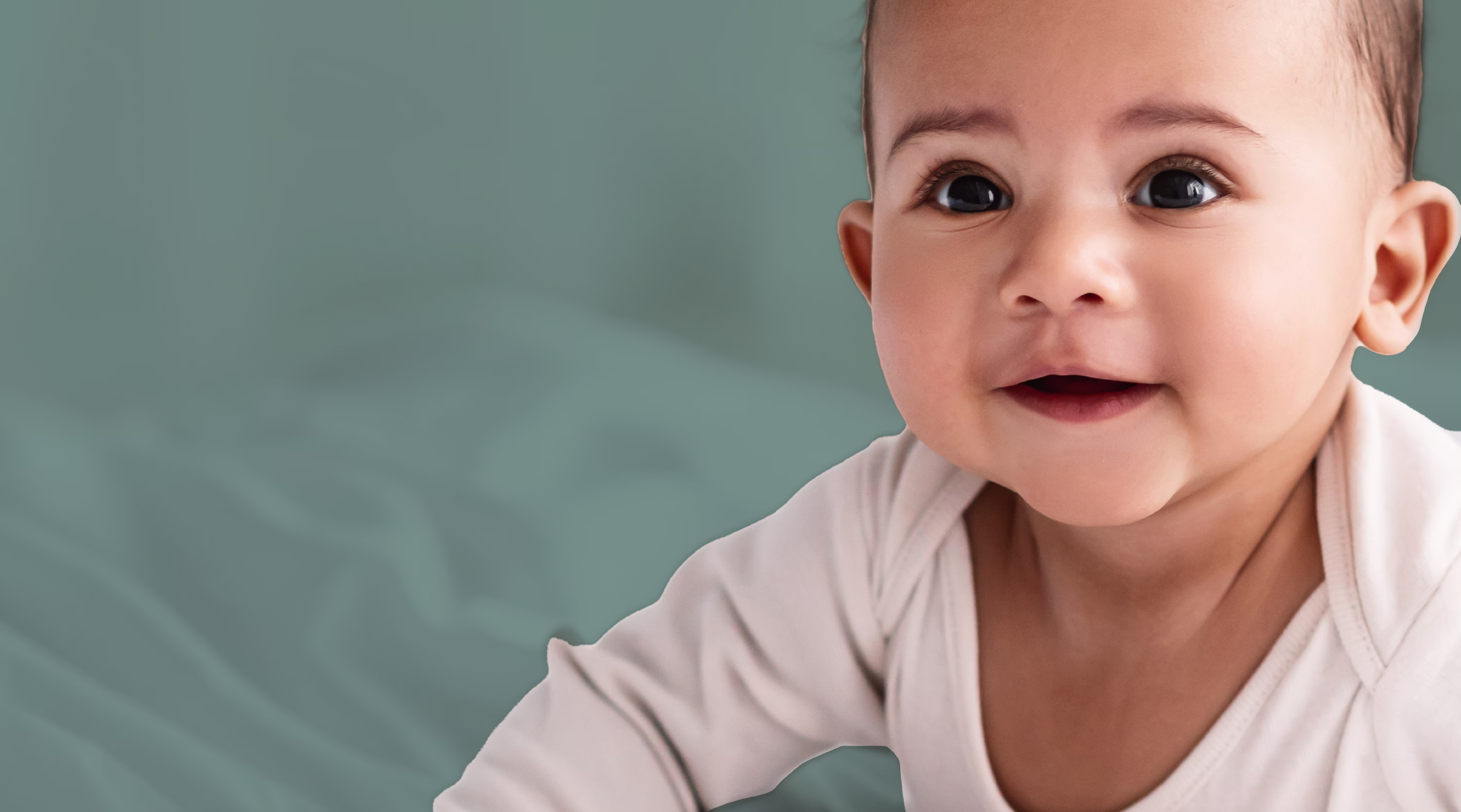 Close up of baby laying on stomach smiling and wearing a cream onesie with sage background