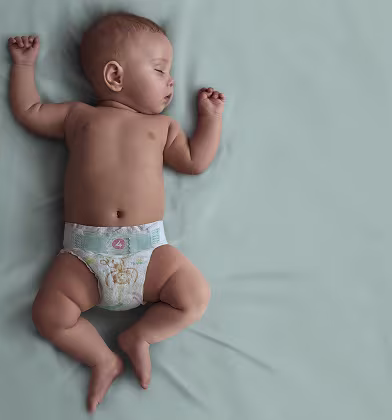 Un bebeluș în scutec Pampers doarme pe spate pe o pătură turcoaz. Un bebeluș în scutec Pampers doarme pe spate pe o pătură turcoaz.