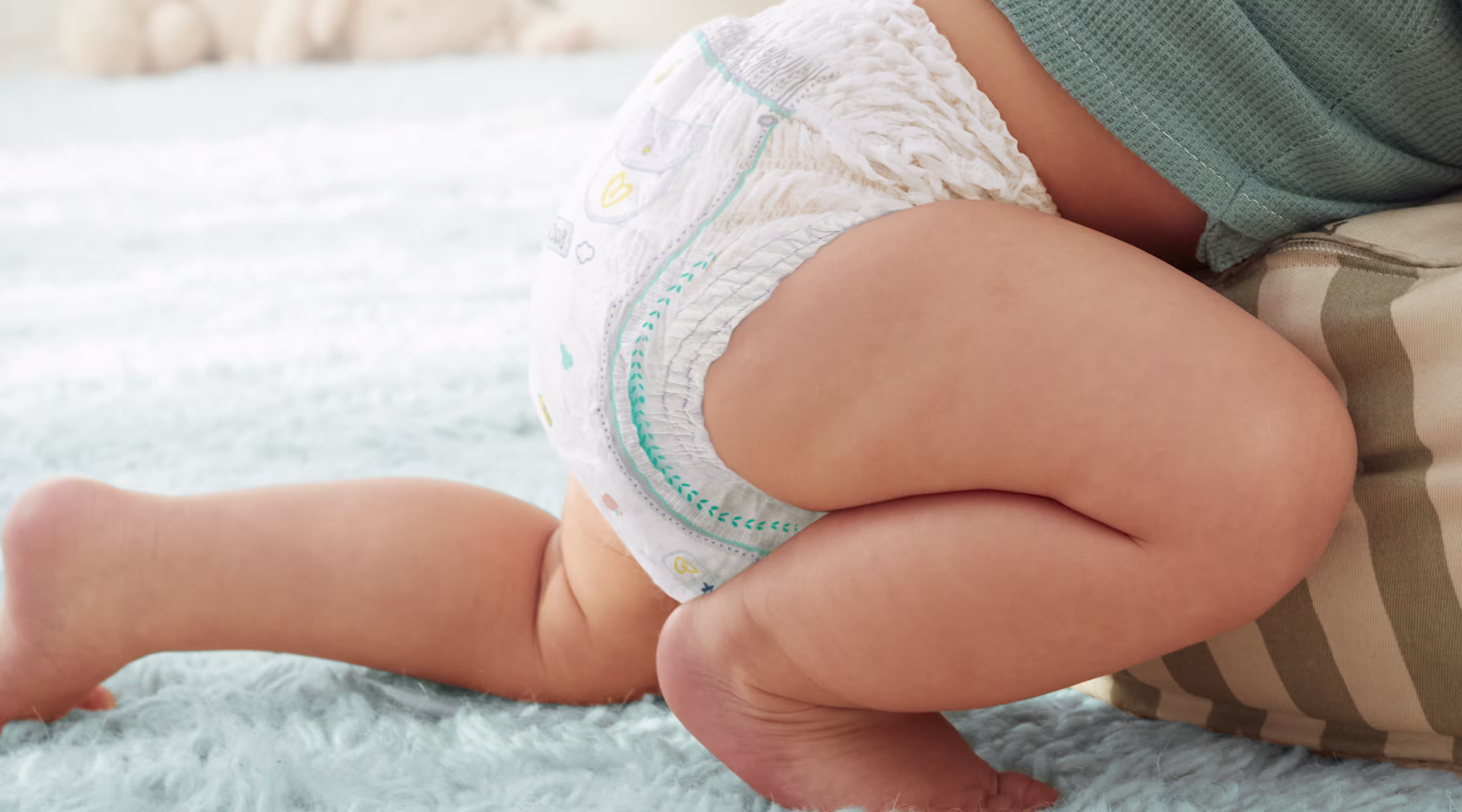 Een baby die een Pampers Pants draagt kruipt over een blauw tapijt. De anti-lekbarrières rond de benen worden benadrukt.