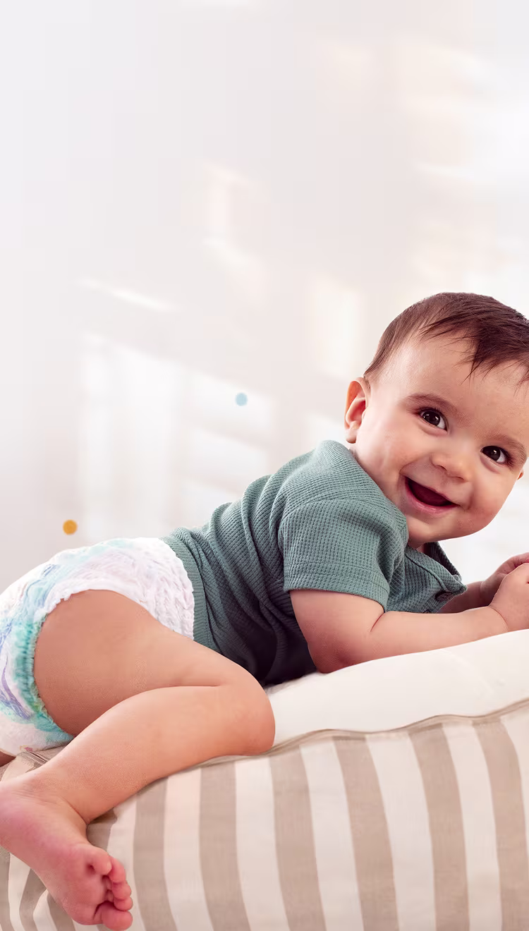 Un bébé portant une couche culotte sourit à la caméra, allongé sur le ventre sur un coussin rayé.