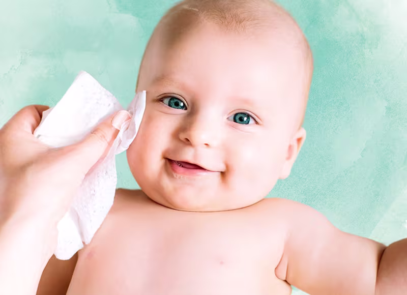 Zbliżenie na twarz niemowlęcia, gdy ręka delikatnie wyciera jego policzek chusteczką Pampers Protect & Care.