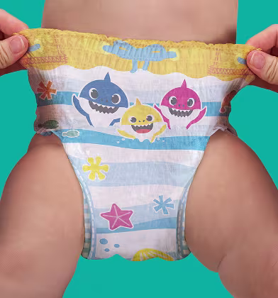 Dvě ruce roztahují boky koupací plenky s motivem Baby Shark na dolní části těla dítěte, ukazujíc pružný pas a celý vzor.