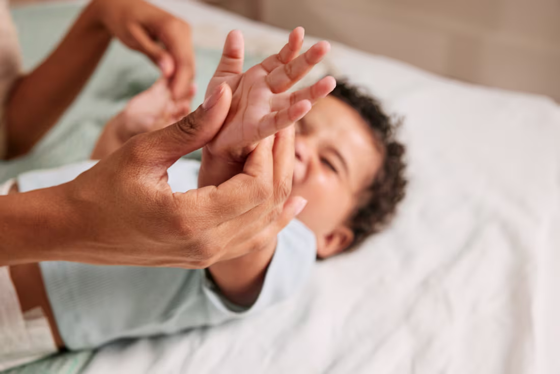 Erwachsener hält sanft die Hand eines liegenden Babys.