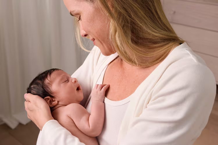 Une mère berce tendrement son nouveau-né en couche contre sa poitrine, le regardant avec douceur.