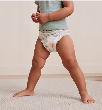 Toddler wearing teal shirt standing with legs spread out, showing off the front of a Pampers Cruisers 360 pull on diaper