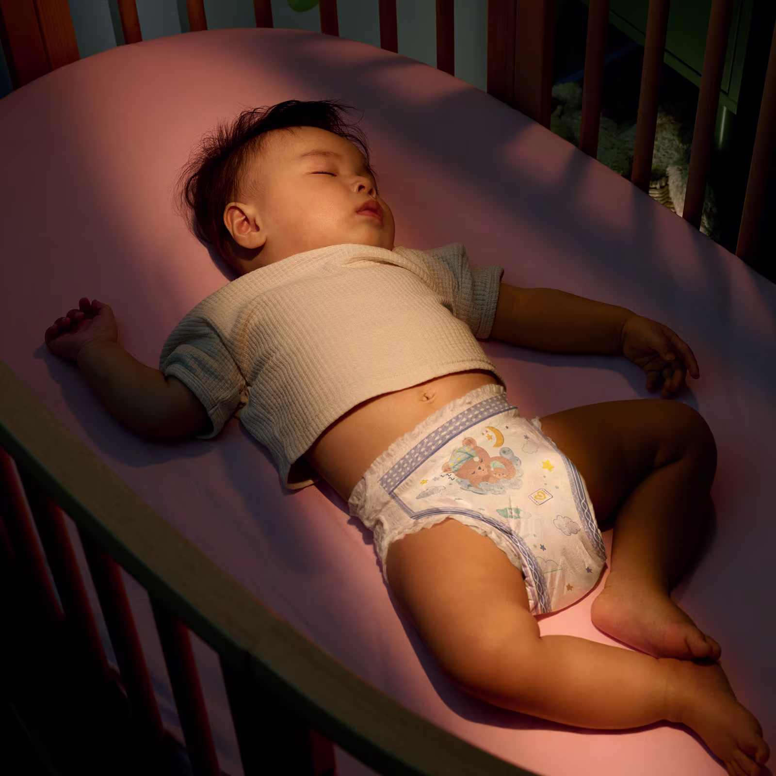 Een kind met een beige t-shirt en een Pampers Pants slaapt vredig op een roze deken. Een kind met een beige t-shirt en een Pampers Pants slaapt vredig op een roze deken.