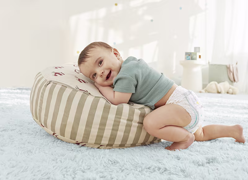 Un copil în scutec stă în genunchi, sprijinindu-se pe mâini și pe genunchi.