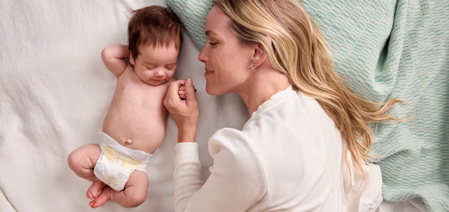 Image of a baby lying on their back with their mother next to them.