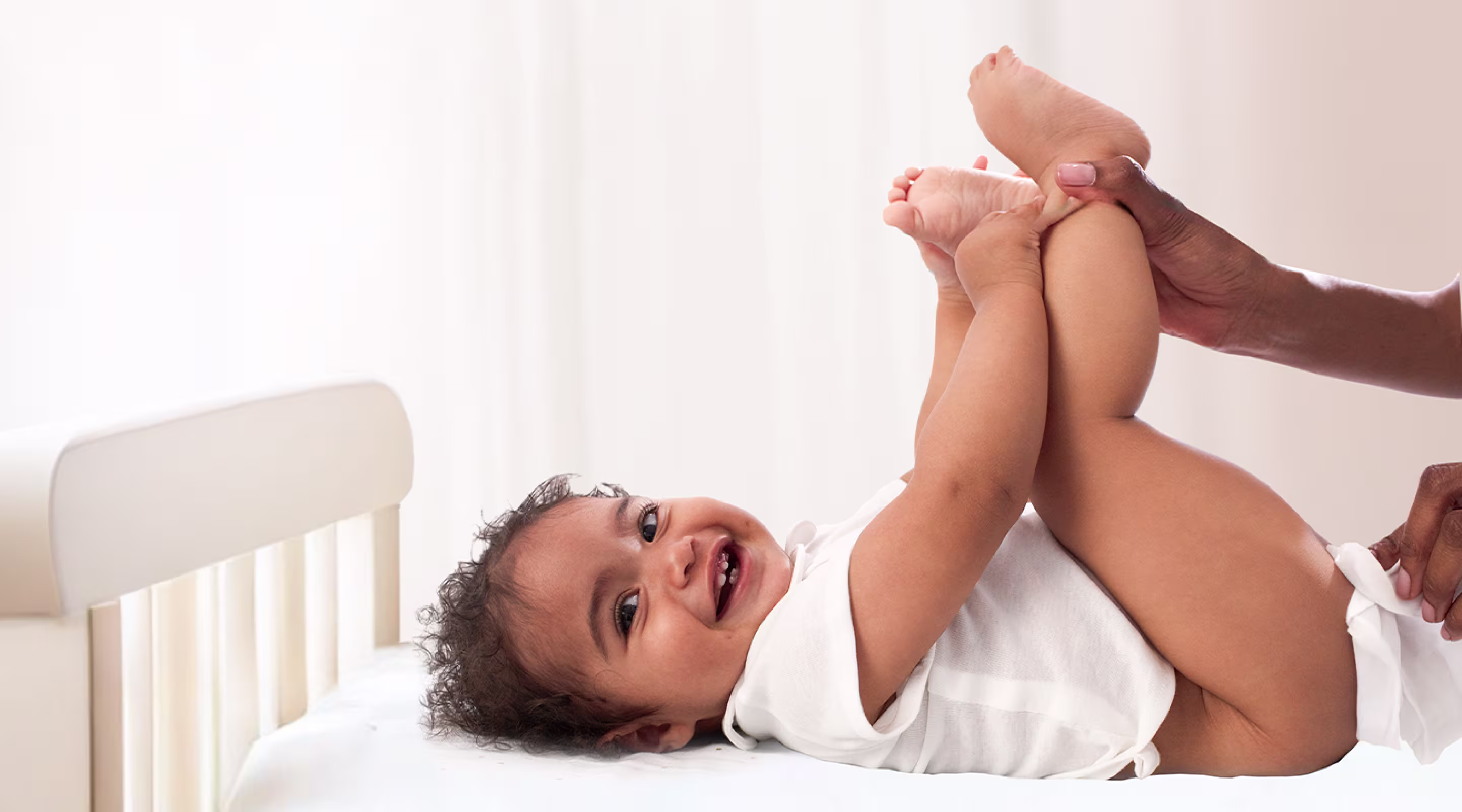 Un bebé está tumbado de espaldas sobre una superficie blanca, levantando los pies mientras un padre utiliza una toallita para limpiar el trasero del bebé.