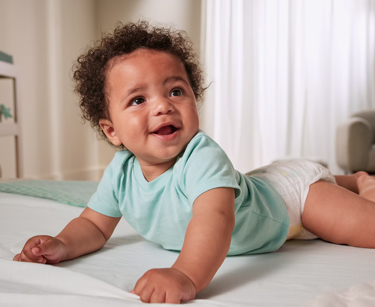 Smiling baby laying on their belly wearing a teal shirt, pushing up with their hands