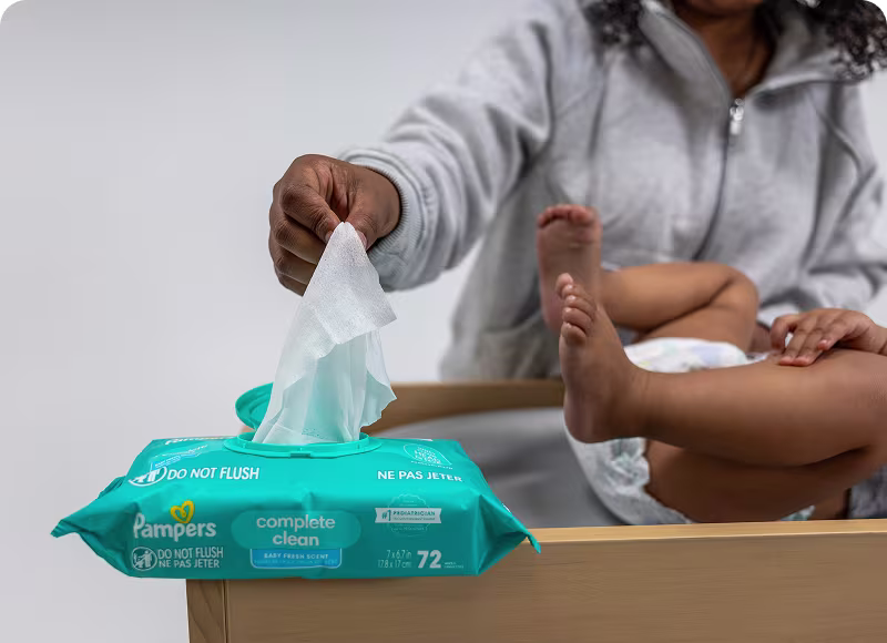 Una madre saca suavemente una toallita Pampers Complete Clean del paquete, lista para asegurar la comodidad de su bebé durante el cambio de pañal. Una madre saca suavemente una toallita Pampers Complete Clean del paquete, lista para asegurar la comodidad de su bebé durante el cambio de pañal.