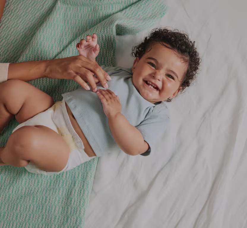 Closeup of baby smiling at camera playing wih the parents hands and wearing pampers diapers