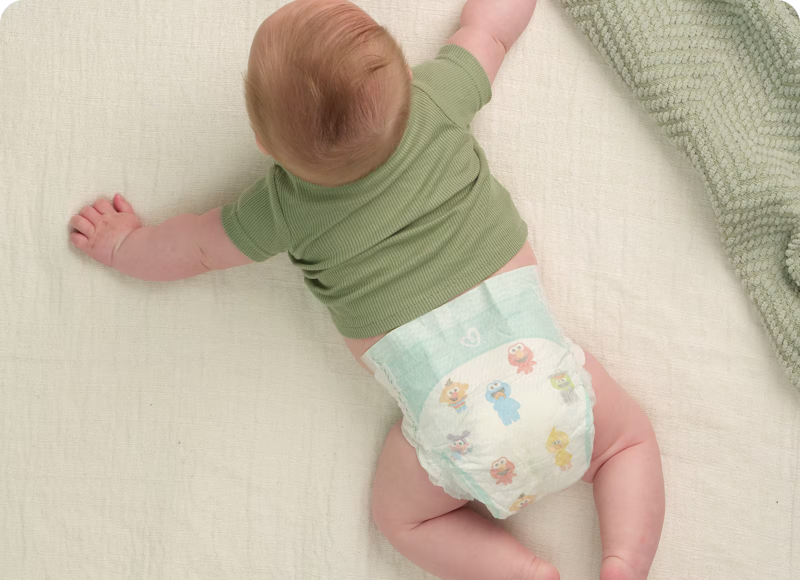 Imagen aérea de un bebé acostado sobre una manta suave color crema, usando un pañal Pampers Baby Dry y una camiseta verde. Imagen aérea de un bebé acostado sobre una manta suave color crema, usando un pañal Pampers Baby Dry y una camiseta verde.
