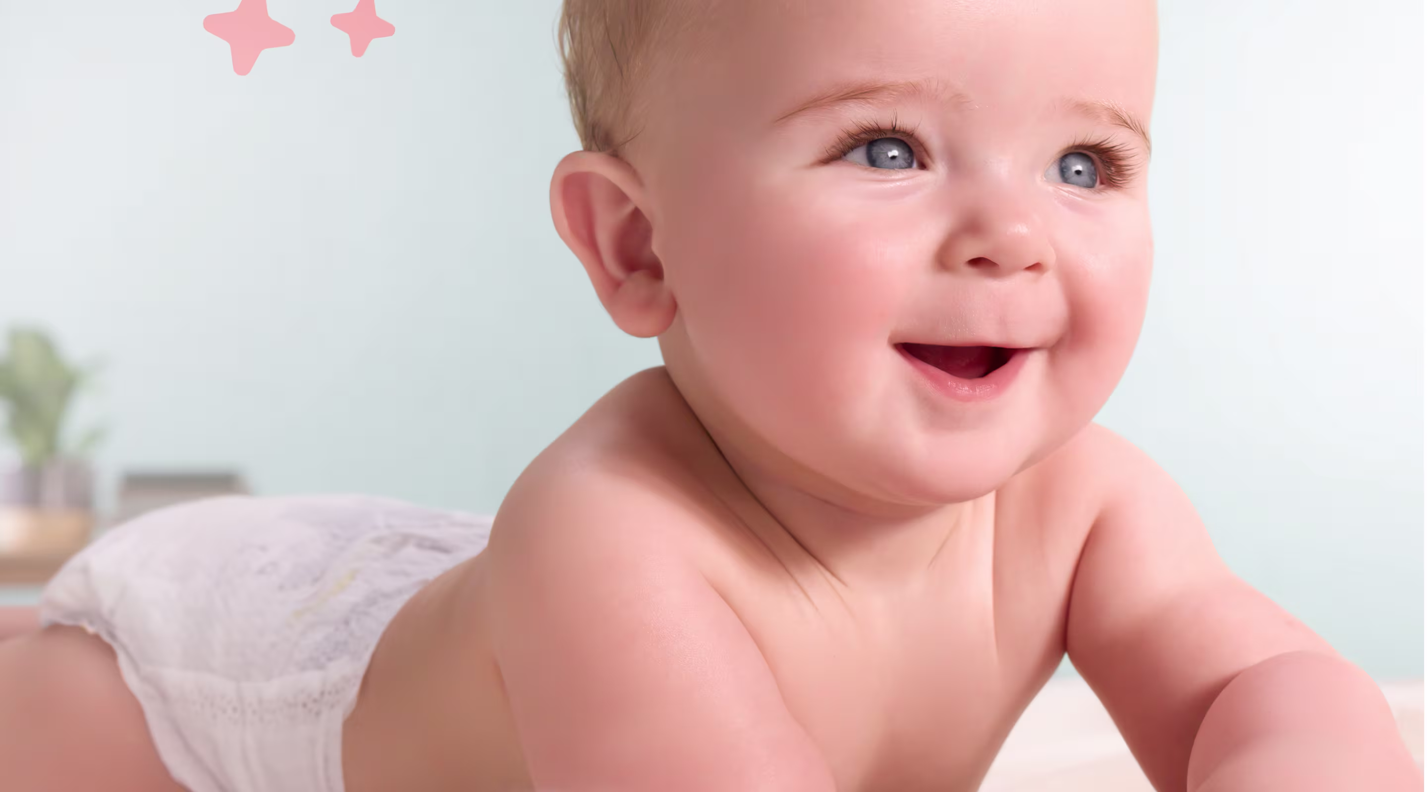 Un bebé feliz con ojos azules que lleva un pañal blanco está tumbado boca abajo y sonríe mientras mira hacia arriba y hacia un lado.