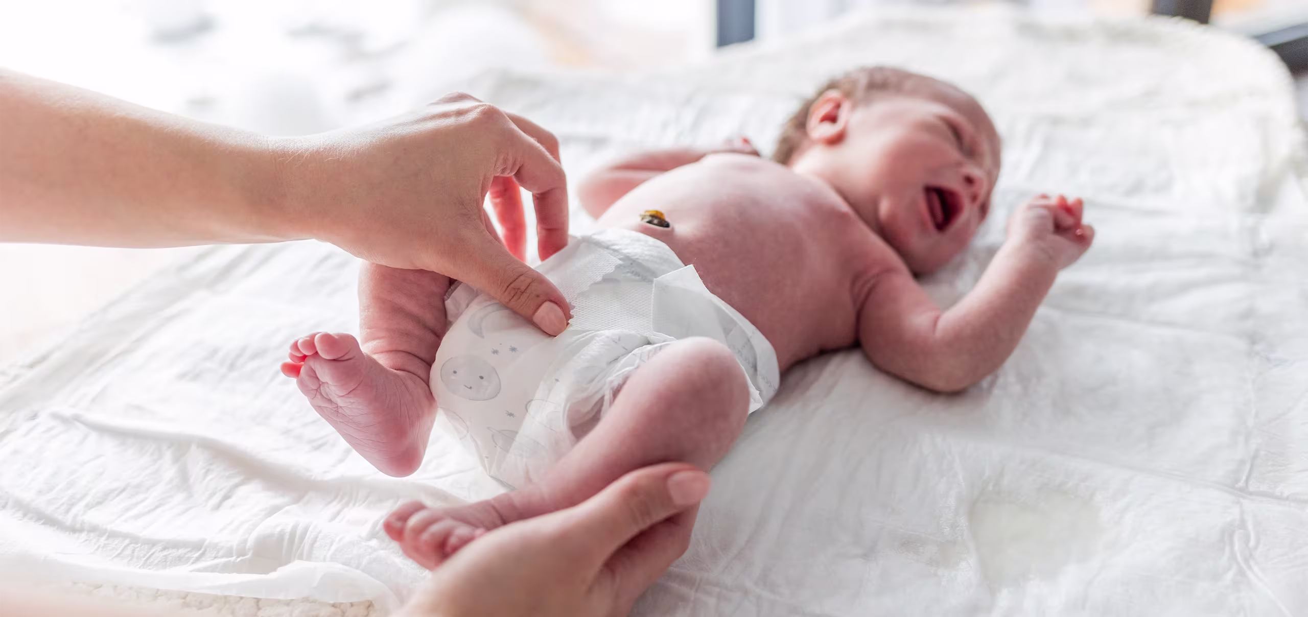 Um bebê recém-nascido deitado em um trocador enquanto seu cuidador troca a fralda