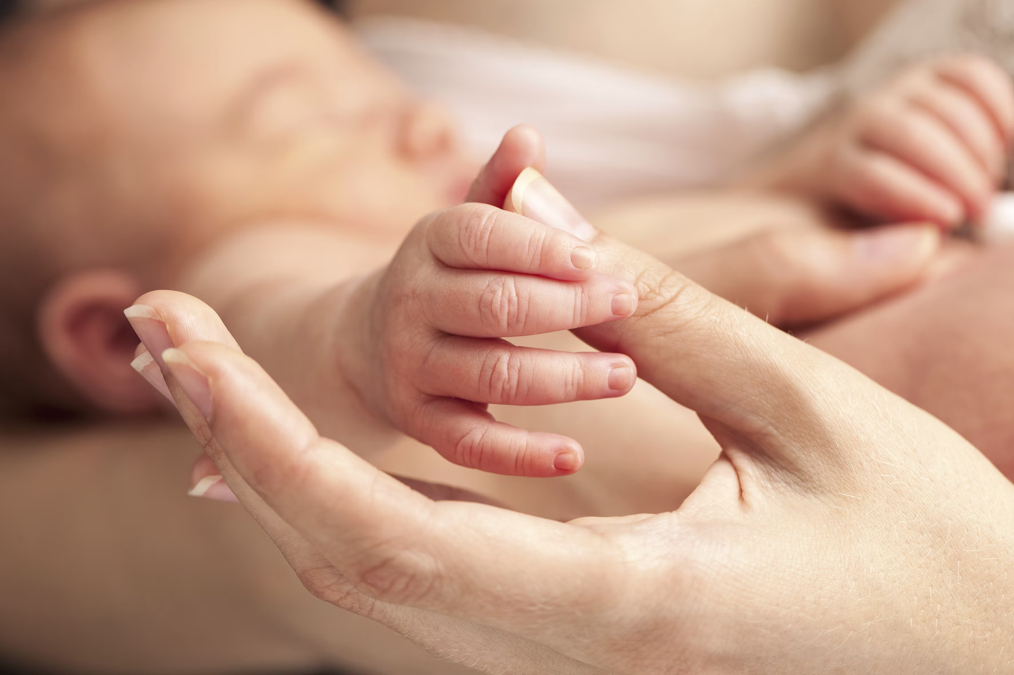 Baby holding their mom's thumb while being cradled by their mom.