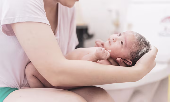 Un adulte tient un nouveau-né couvert de vernix dans ses bras, dans une salle de bain lumineuse.
