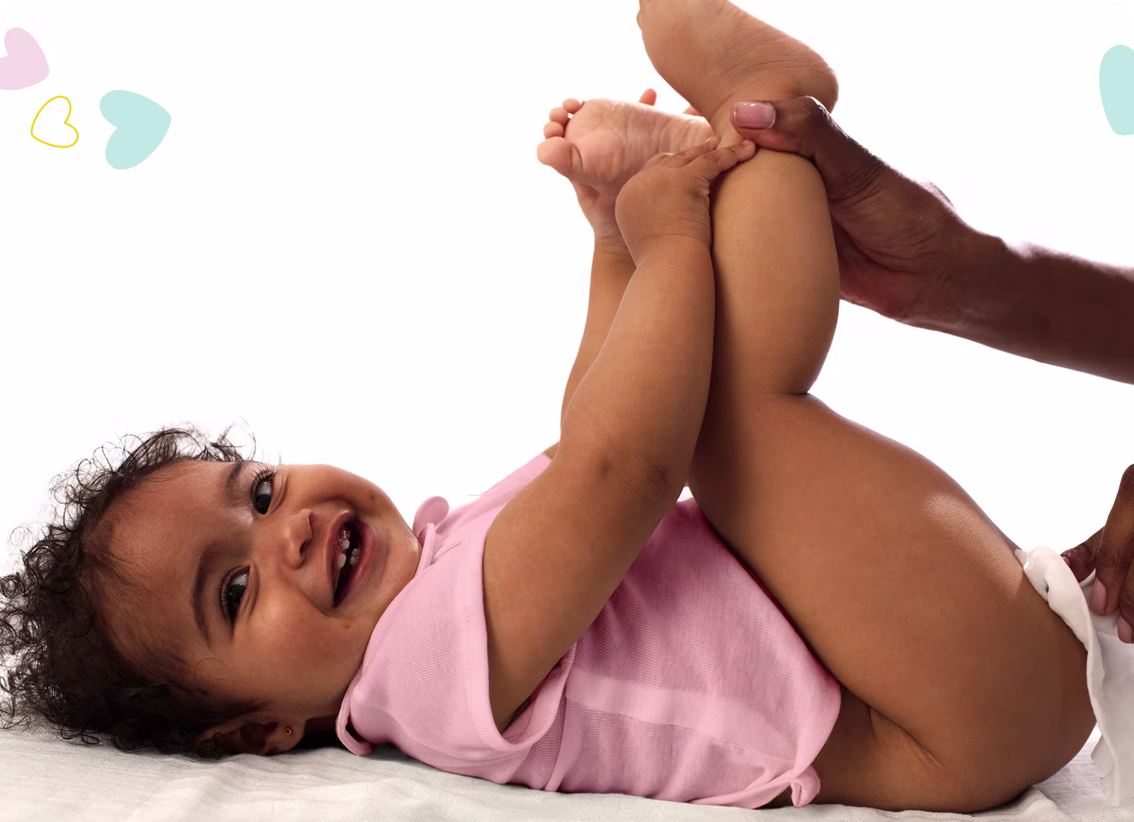 Un bebé está tumbado de espaldas sobre una superficie blanca, levantando los pies mientras un padre utiliza una toallita para limpiar el trasero del bebé.