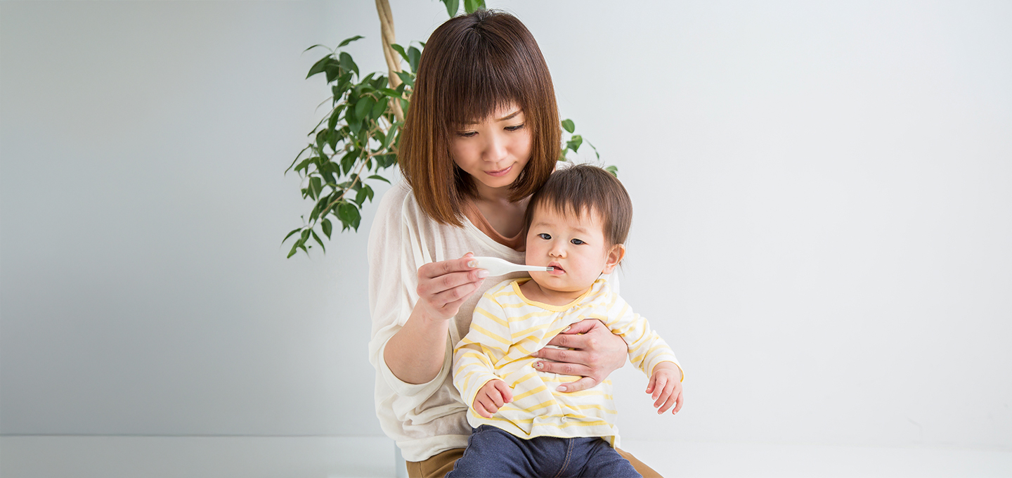 Madre sentada sostiene a su bebé mientras le ofrece una cucharada de líquido, ilustrando cuidado y alimentación durante un episodio de diarrea infantil.