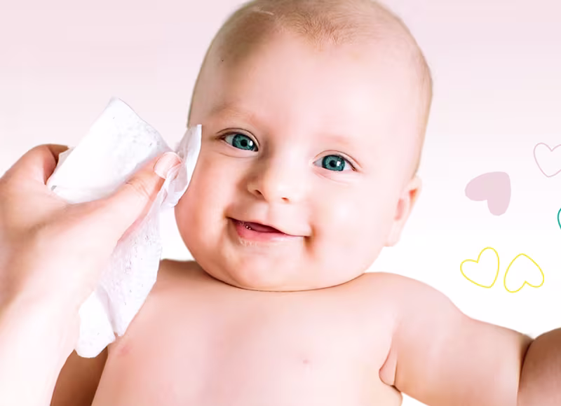 En närbild av ett babys ansikte medan en hand försiktigt torkar deras kind med en Pampers Sensitive babyservett.