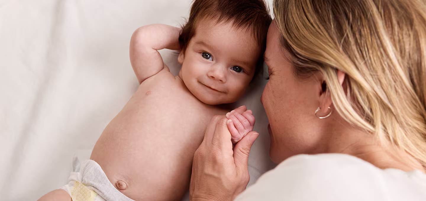 Una madre juega con su bebé feliz, que lleva un pañal Pampers, destacando la seguridad