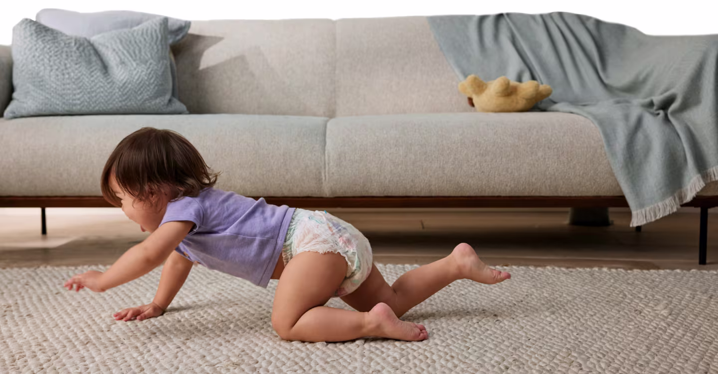 Dziecko raczkuje po szarym dywanie. W tle widać szarą sofę.